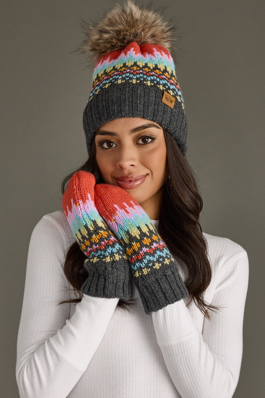 Woman wearing a colorful knit hat and mittens against a gray background