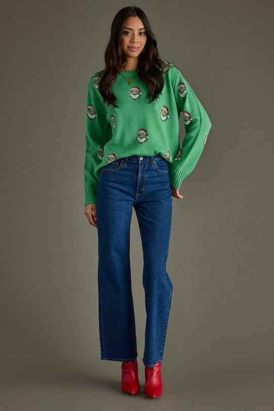 Woman wearing a green sweater with Santa pattern and blue jeans on a gray background