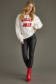 Woman wearing a white sweater with 'Holly Jolly' text, black pants, and red boots on a gray background