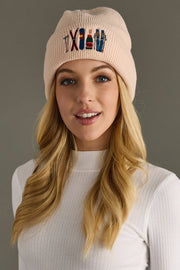 Woman wearing a blush beanie with colorful text and designs on a gray background