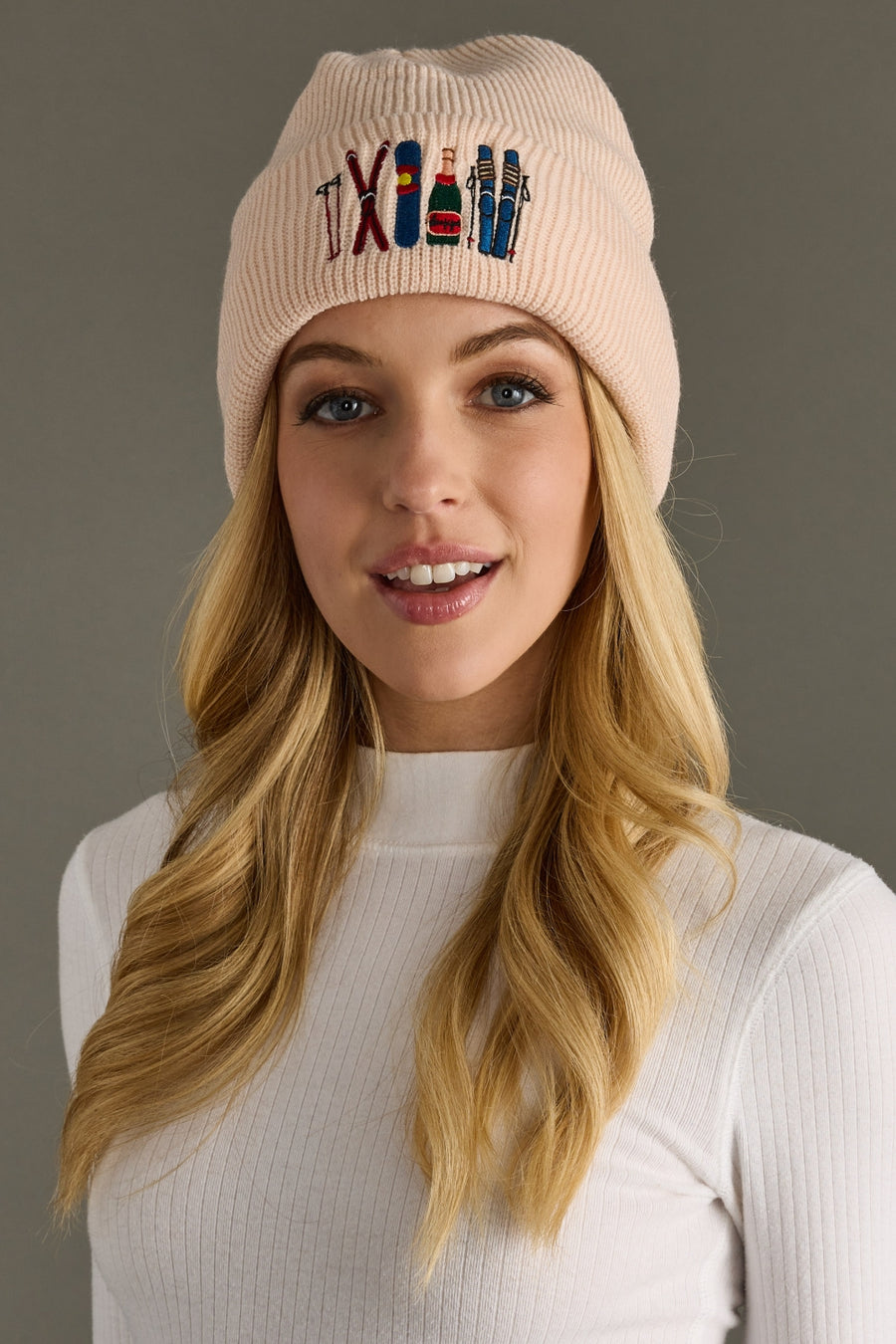 Woman wearing a blush beanie with colorful text and designs on a gray background
