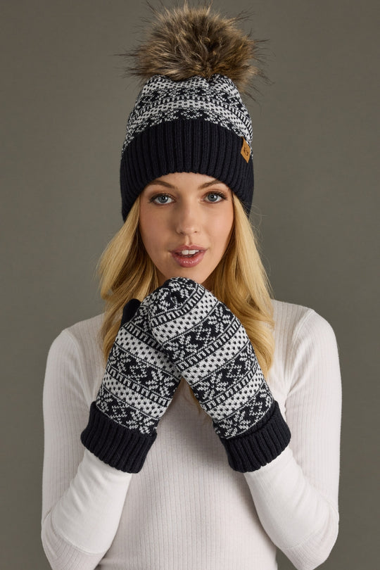 Person wearing a dark navy and white patterned beanie and mittens against a gray background