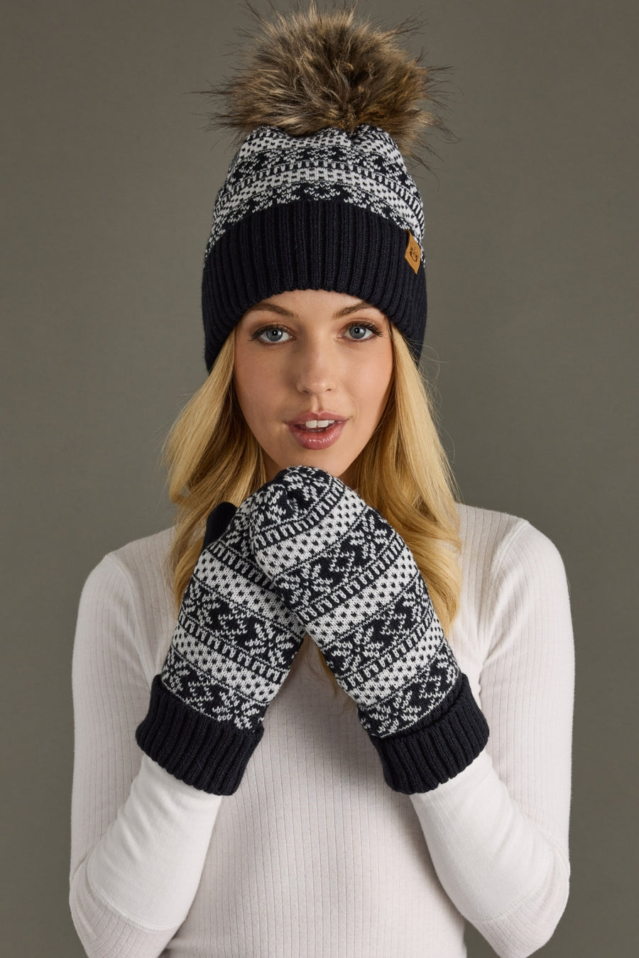 Person wearing a dark navy and white patterned beanie and mittens against a gray background