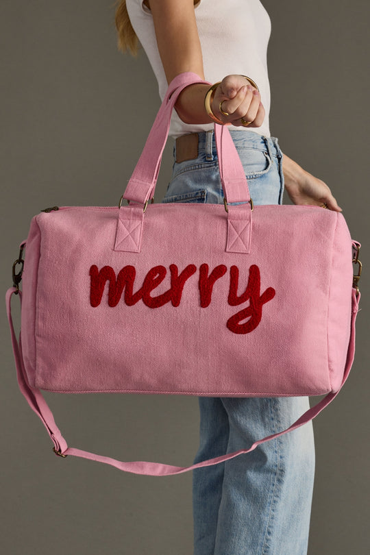 Pink duffel bag with 'merry' text held by a person against a neutral background