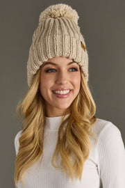 Woman wearing a beige knitted beanie with a pom-pom against a gray background