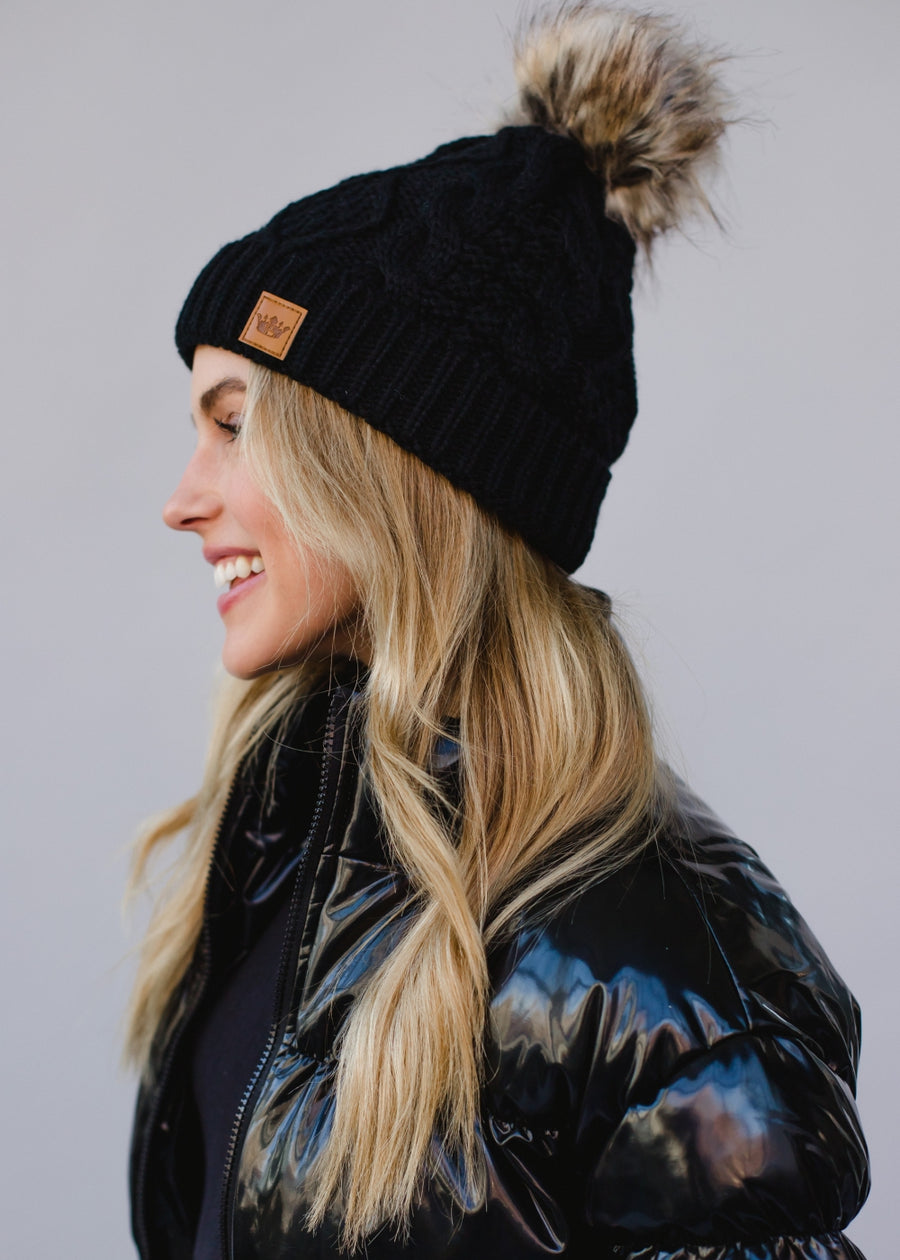Woman wearing a black knit beanie with a pom-pom on a plain background