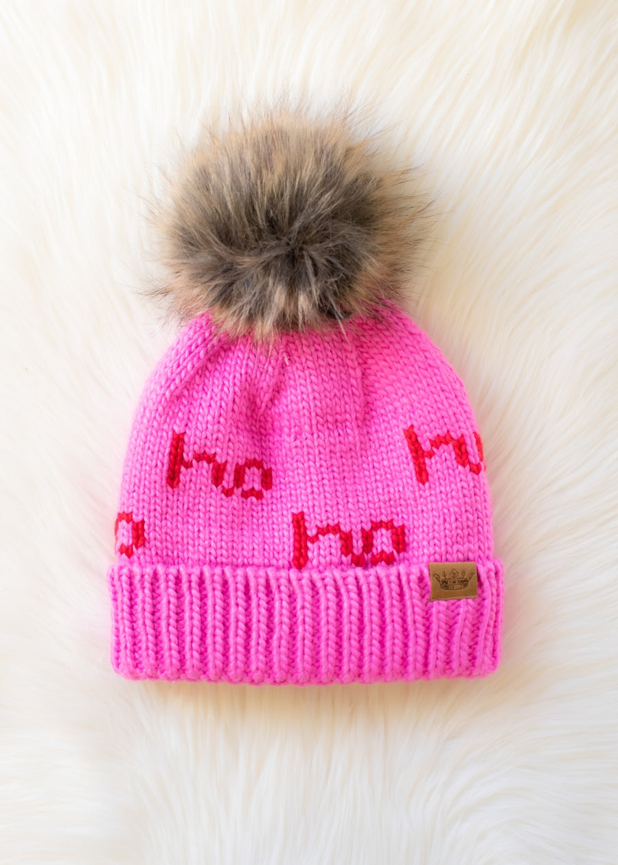 Pink knit hat with red text and fur pom-pom on a white background