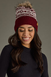 Woman wearing a patterned beanie with a fur pom-pom on a gray background