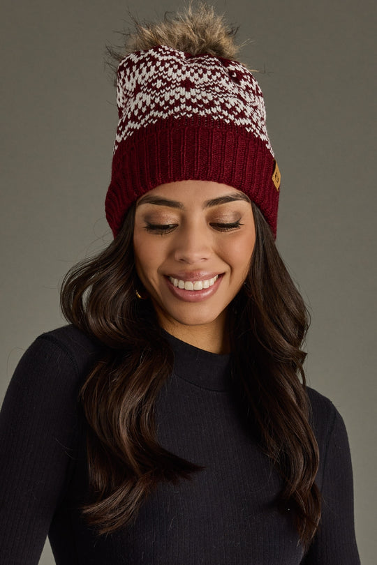 Woman wearing a patterned beanie with a fur pom-pom on a gray background