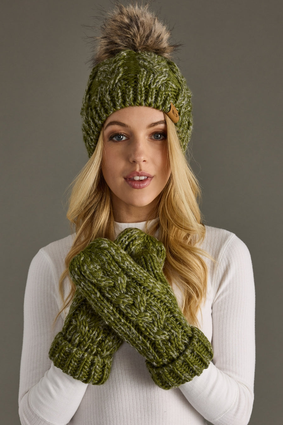 Woman wearing a green knitted beanie and gloves against a gray background