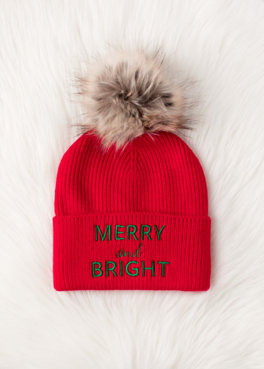 The Panache Apparel Collection Merry & Bright Pom Hat - Red & Green features a cozy fleece lining, large faux fur pom-pom, and green and gold "Merry and Bright" embroidery that stands out on the vibrant red knit.