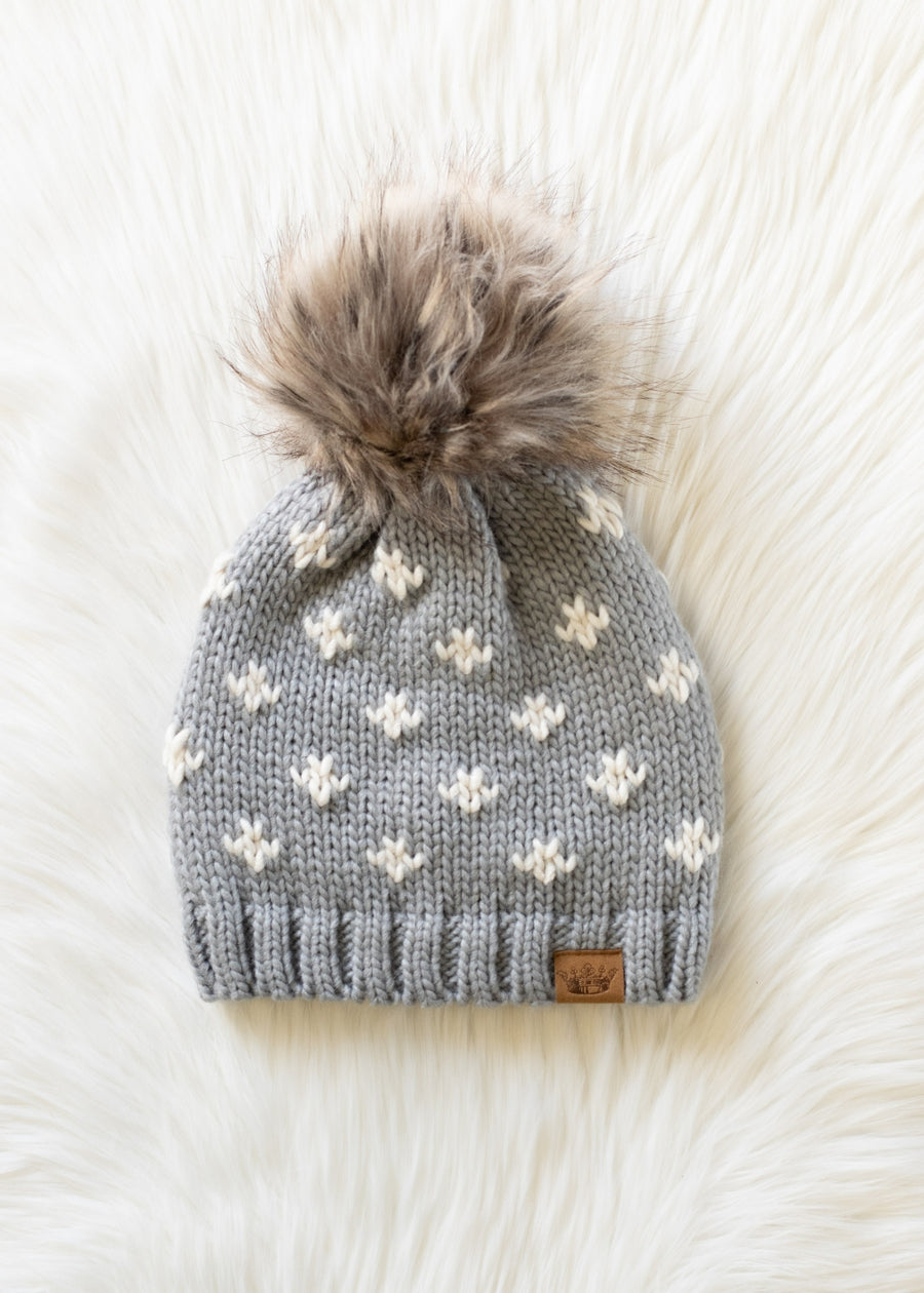 Gray knit beanie with white floral patterns and a fluffy pom-pom on a white background