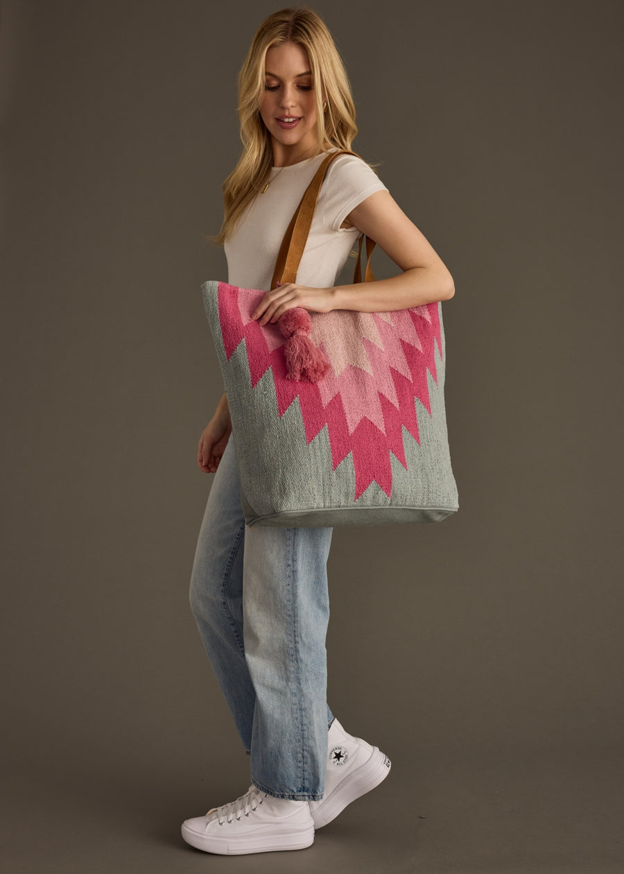 Woman holding a tote bag with a pink and gray design against a plain background