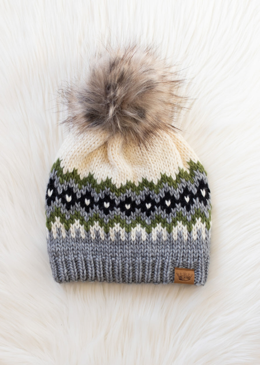 Knit beanie with a patterned design and fur pom-pom on a light wooden surface.