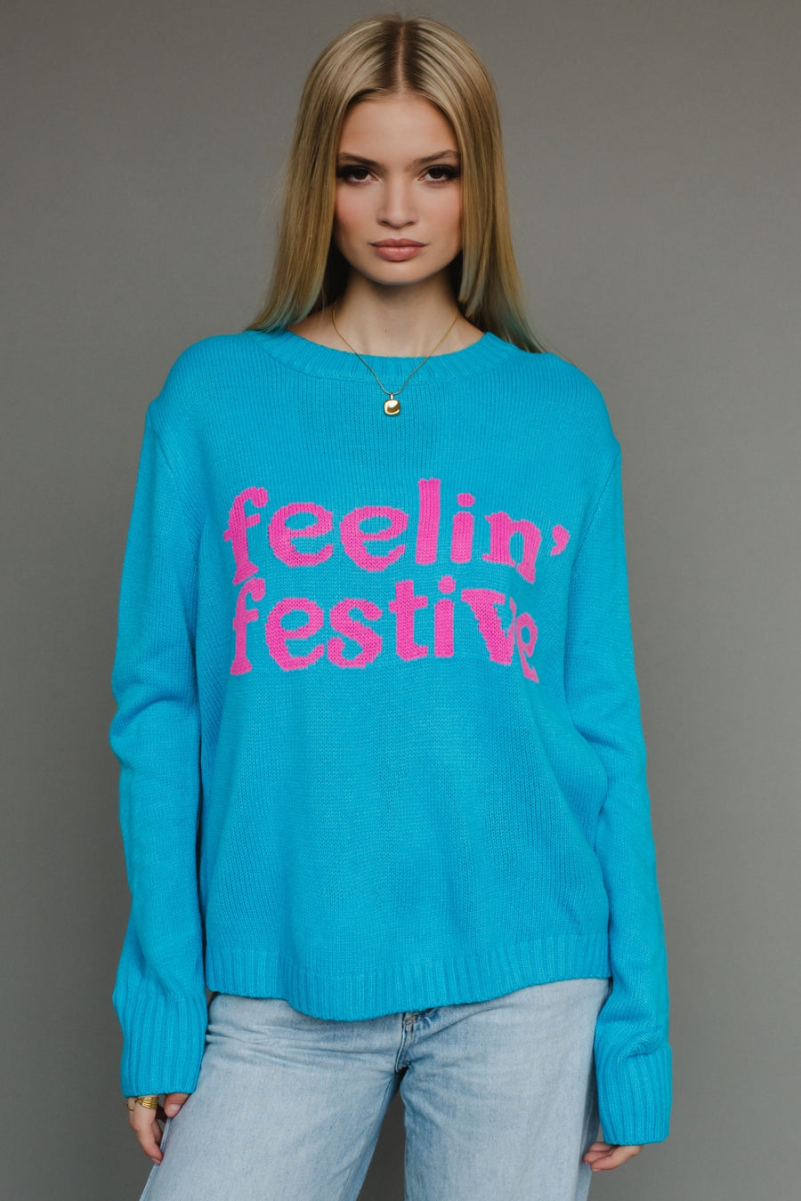 Woman wearing a blue sweater with 'feelin' festive' text against a gray background