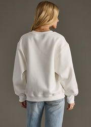 Person wearing a white sweatshirt and light blue jeans against a gray background