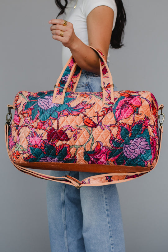 Person holding a colorful floral-patterned handbag against a gray background