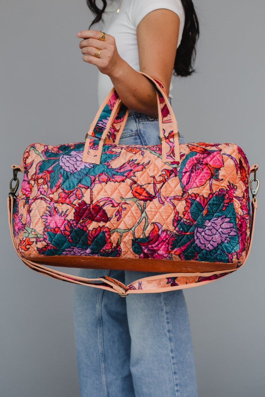 Person holding a colorful floral-patterned handbag against a gray background
