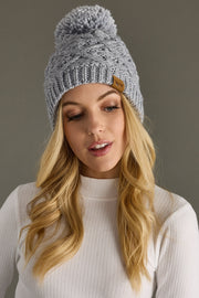 Woman wearing a gray knit beanie with a pom-pom against a neutral background