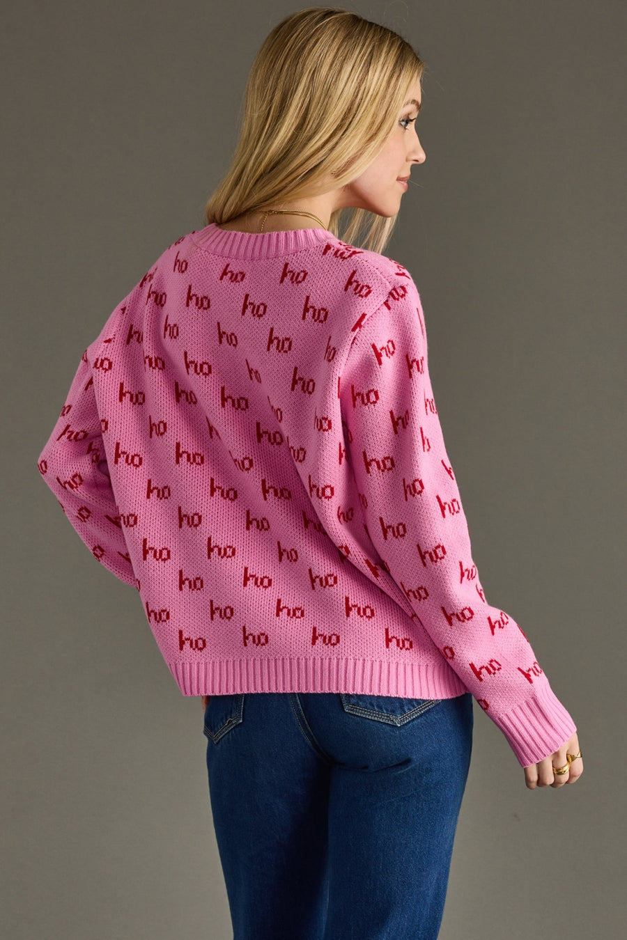 Person wearing a pink sweater with 'ho ho ho' pattern on a gray background