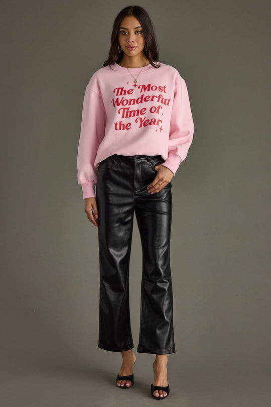 Woman wearing a pink sweater with text and black leather pants on a gray background
