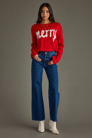 Woman wearing a red sweater with 'merry' text and blue jeans on a gray background