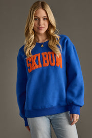 Woman wearing a blue sweatshirt with 'SKI BUM' text on a gray background