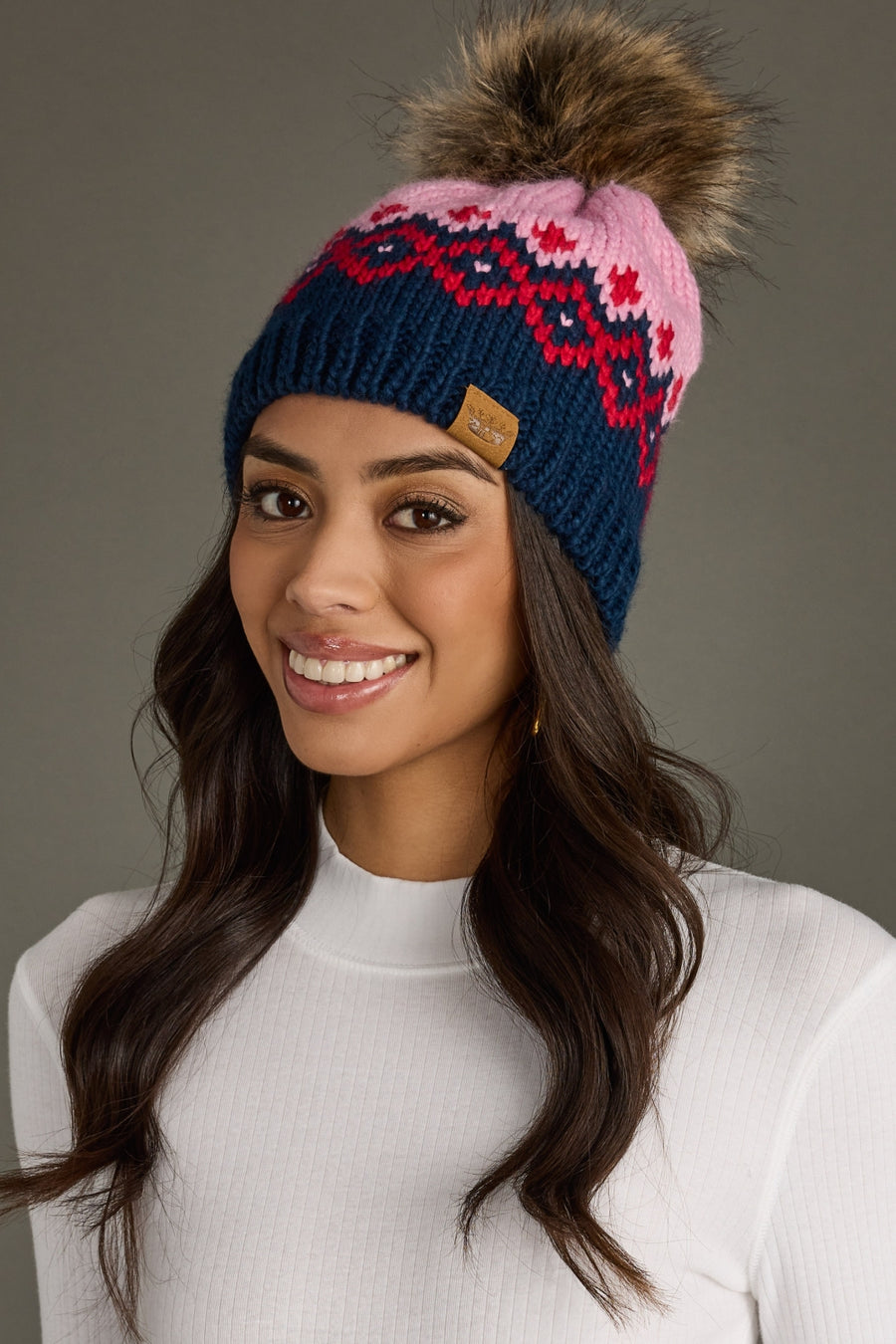 Woman wearing a colorful knit beanie with a pom-pom on a gray background