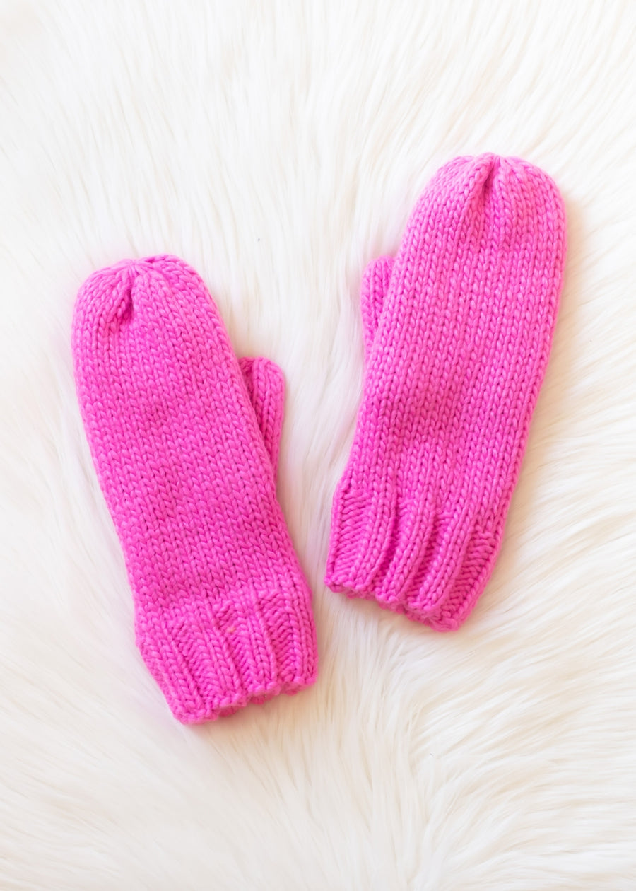 Pair of pink knitted mittens on a white fur surface