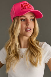 Woman wearing a bright pink cap with 'APRES' text on a gray background