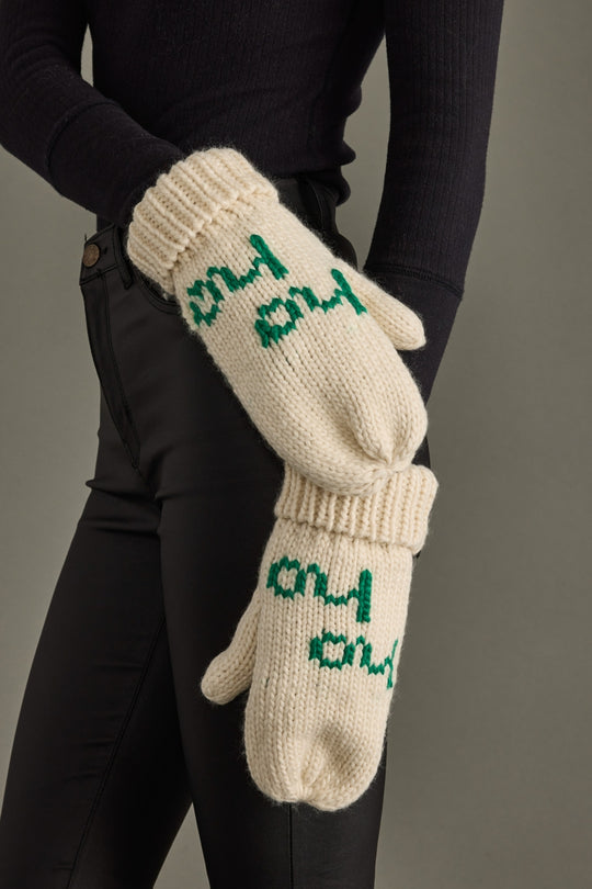 Pair of white knit gloves with green text held by a person against a gray background