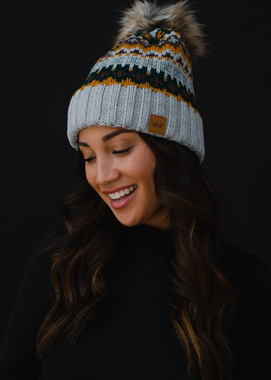 Woman wearing a patterned beanie with a pom-pom against a black background