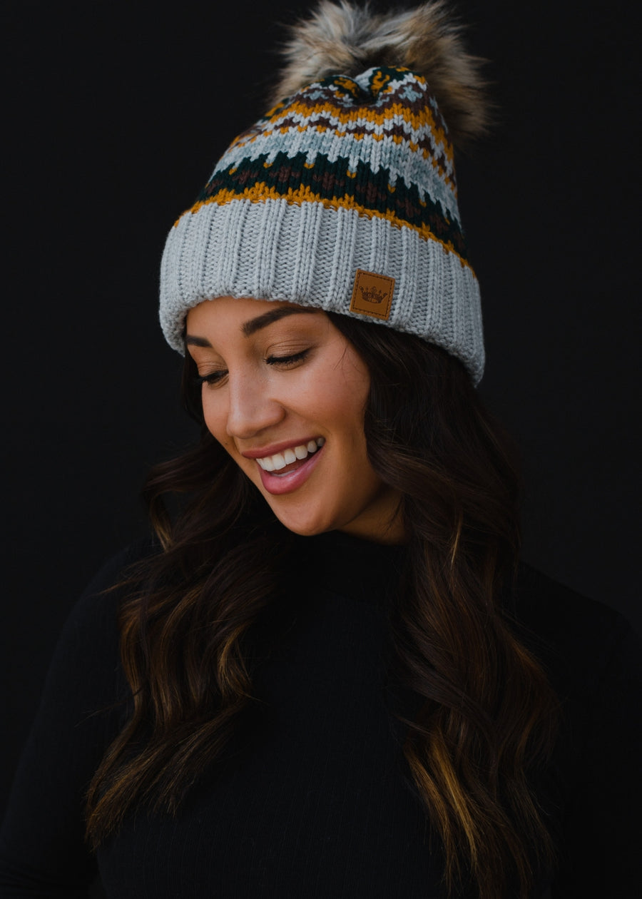 Woman wearing a patterned beanie with a pom-pom against a black background