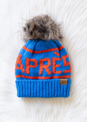Blue knit beanie with orange text and fur pom-pom on a white surface