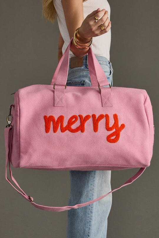 Pink duffel bag with 'merry' text held by a person against a neutral background