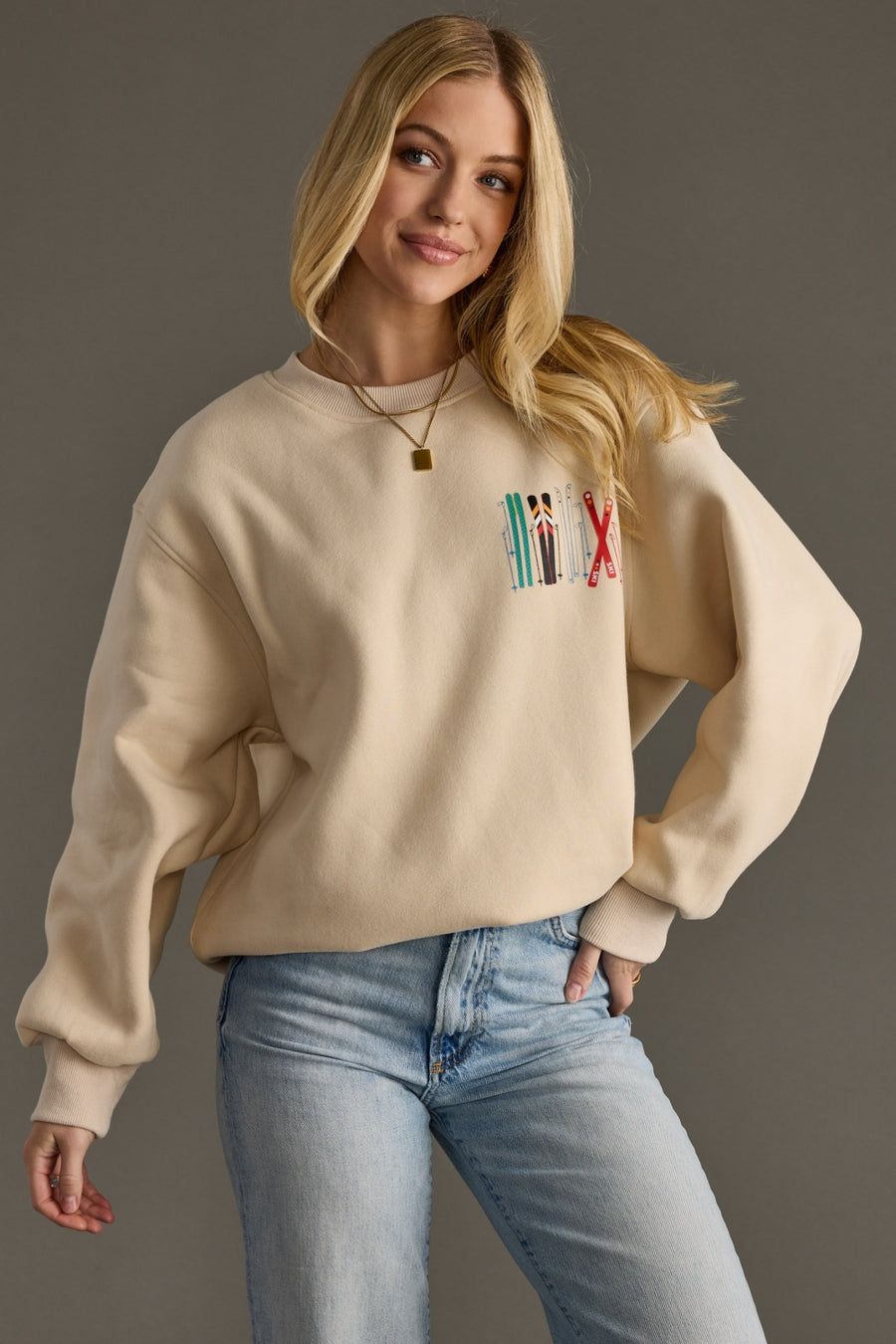 Woman wearing a beige sweatshirt with a colorful graphic on a gray background