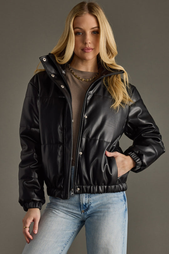 Woman wearing a black leather jacket and light blue jeans against a gray background