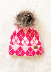 Pink argyle patterned beanie with fur pom-pom on a white fluffy surface