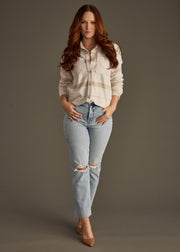 Woman wearing a light-colored shirt and ripped jeans against a gray background