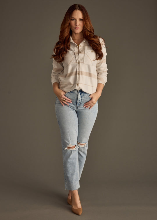 Woman wearing a light-colored shirt and ripped jeans against a gray background