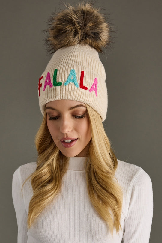 Beige knit hat with colorful 'FALALA' text and fur pom-pom worn by a model against a gray background