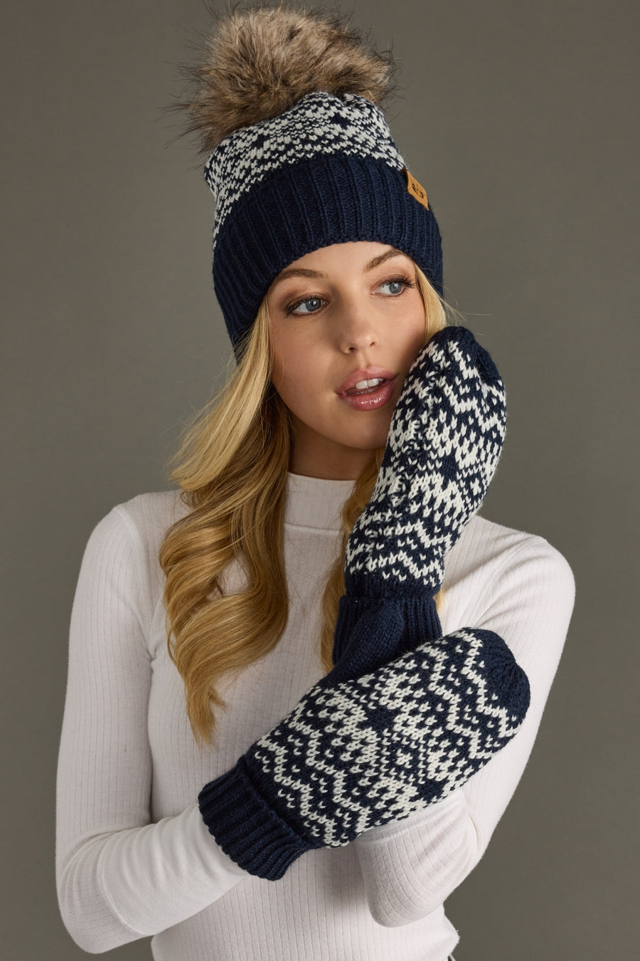 Woman wearing a navy and white patterned beanie and mittens against a gray background