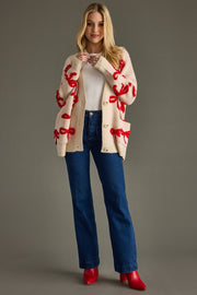 Woman wearing a cream cardigan with red patterns, white shirt, blue jeans, and red shoes on a gray background