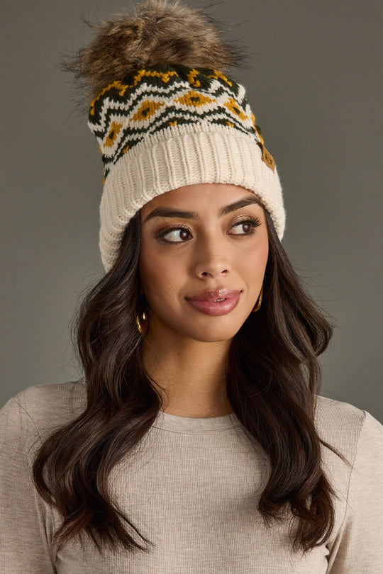 Woman wearing a patterned knit headband with a fluffy pom-pom on a gray background