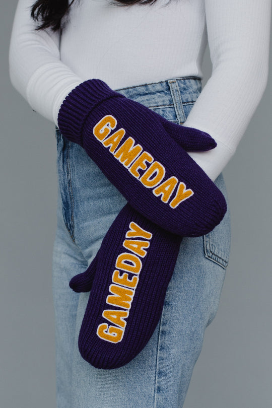 Purple 'GAMEDAY' mittens worn by a person with a gray background