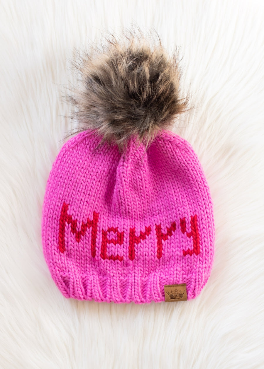 Pink knit beanie with 'Merry' text and fur pom-pom on a white background