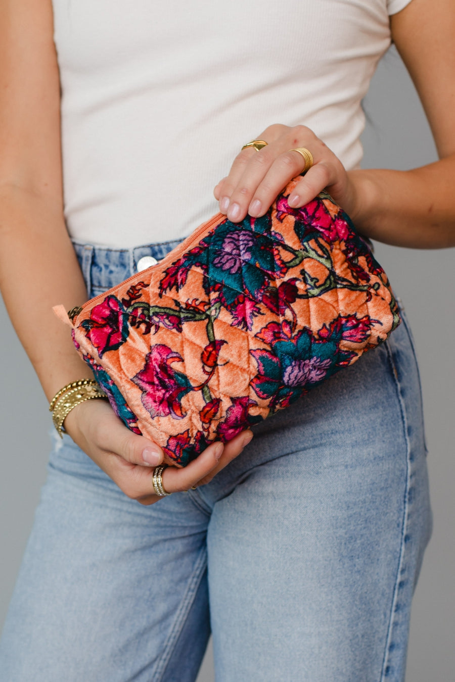 Person holding a colorful floral travel pouch against a neutral background