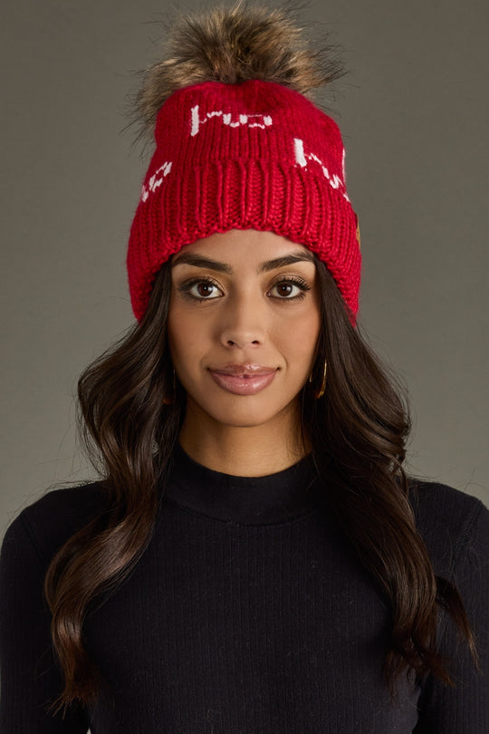 Woman wearing a red knit beanie with a fur pom-pom on a gray background