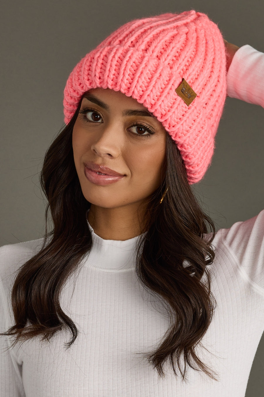 Woman wearing a pink knit beanie with a brand logo on a gray background