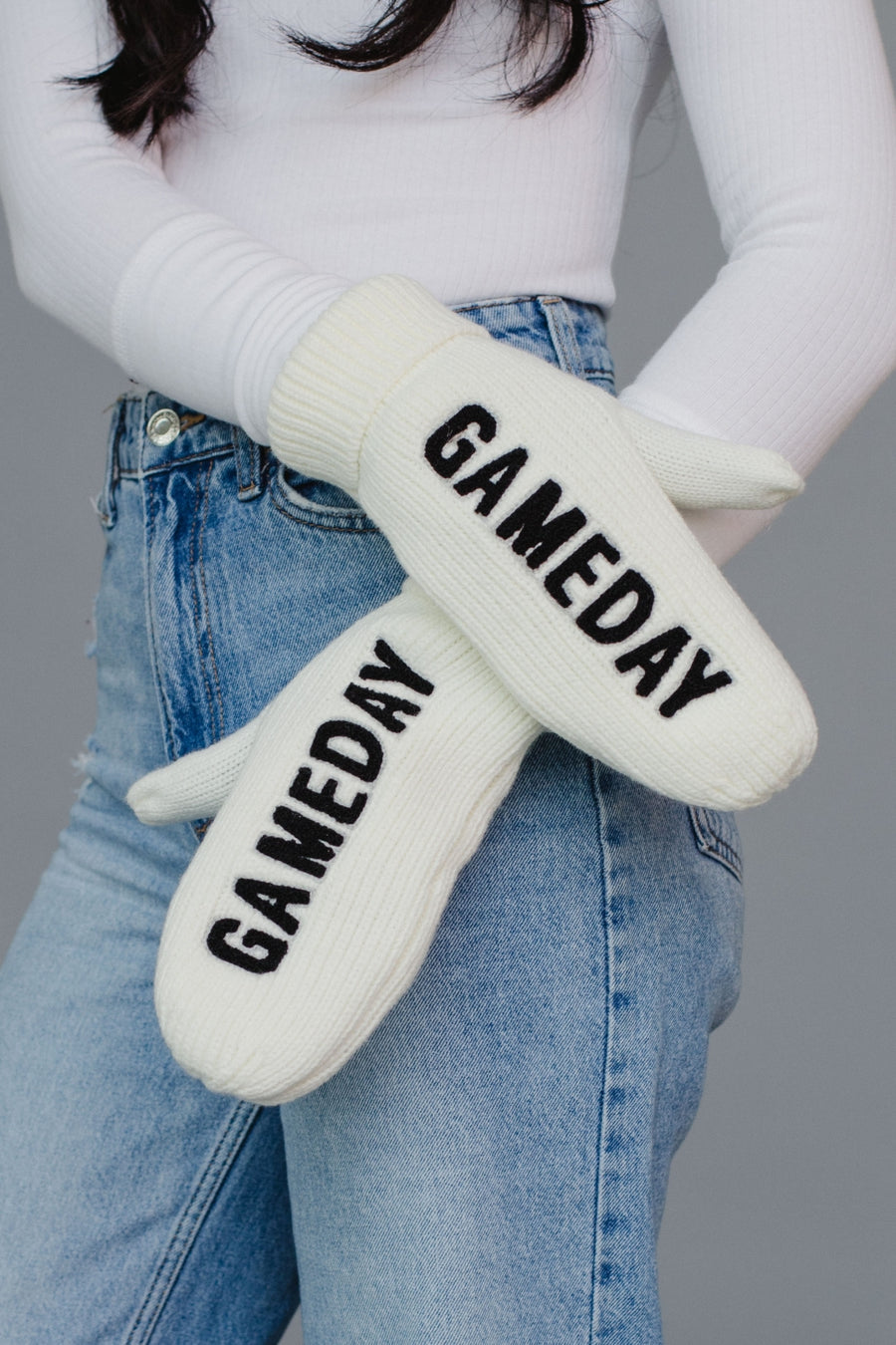White mittens with 'GAMEDAY' text worn by a person wearing jeans and a white long-sleeve shirt.
